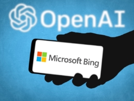Shadowy hand holding a smartphone with Microsoft Bing on it over a blue background with the OpenAI logo